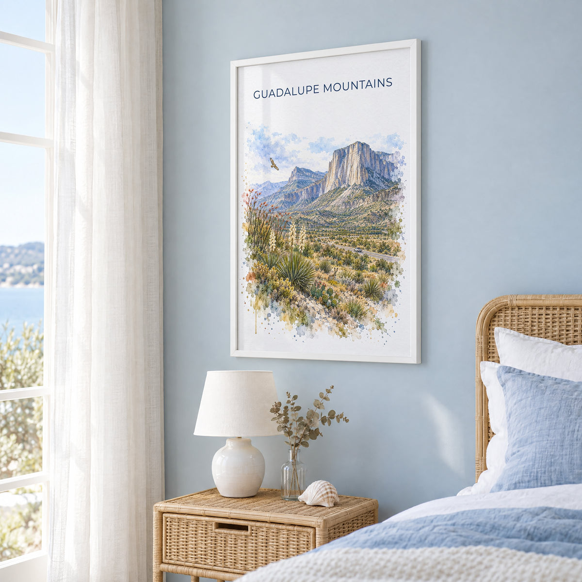 Guadalupe Mountains National Park watercolor in a white frame on a pale blue wall beside a rattan bed in a coastal bedroom