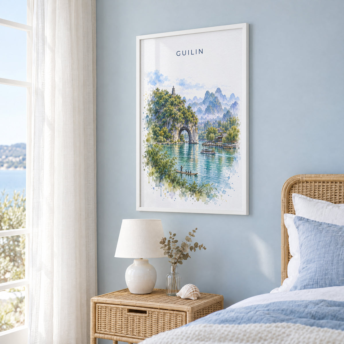 Guilin watercolor print in a white frame on a pale blue wall beside a rattan bed in a coastal bedroom