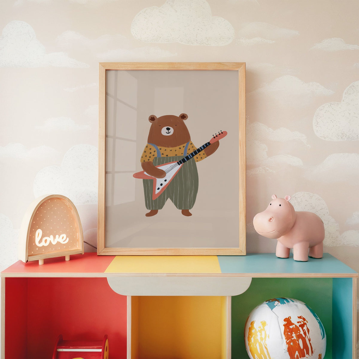 Guitar bear green overalls nursery print in an oak frame on a rainbow toy shelf against cloud wallpaper