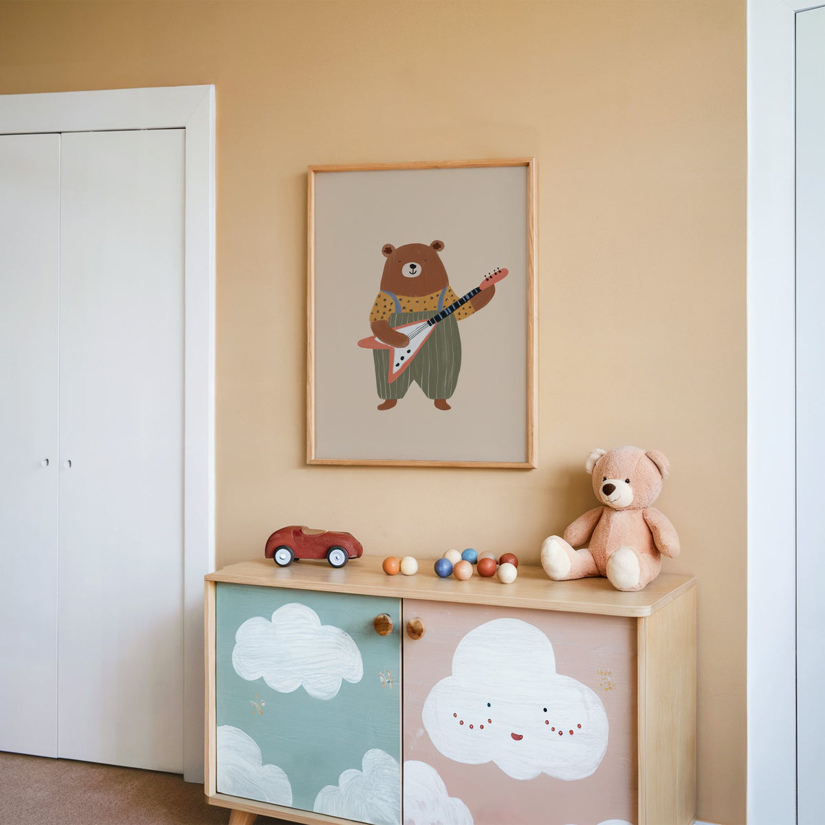 Guitar bear green overalls nursery print in an oak frame on a peach wall above a cloud-painted cabinet