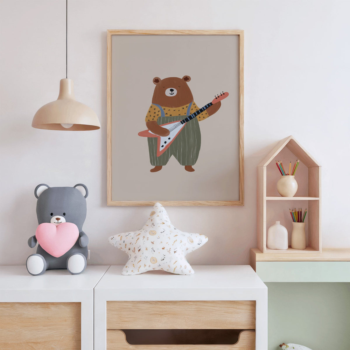 Guitar bear green overalls nursery print in an oak frame above a white dresser with a star pillow and house shelf
