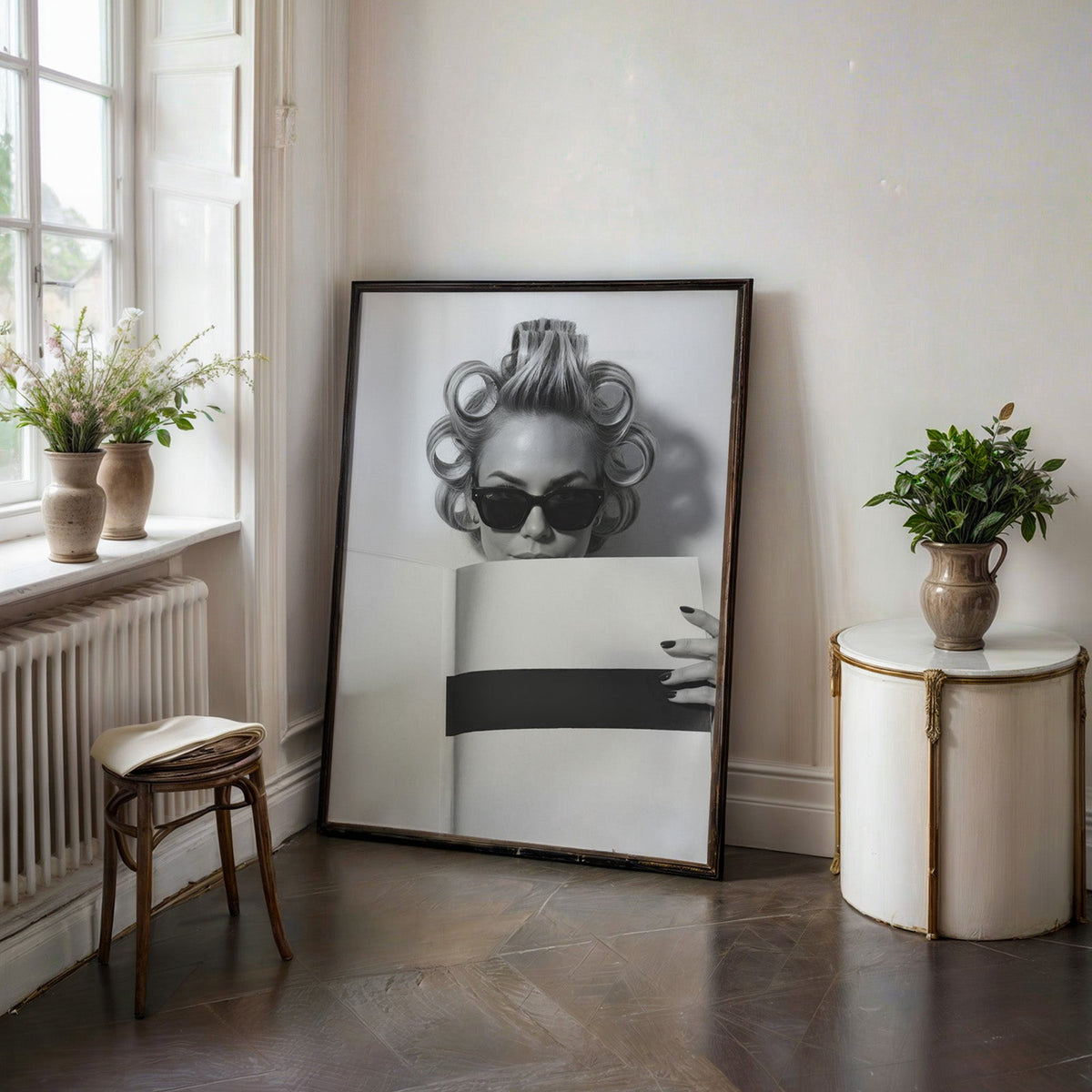 Woman in hair rollers and sunglasses with page print in a black frame on a dark stone floor beside a white side table