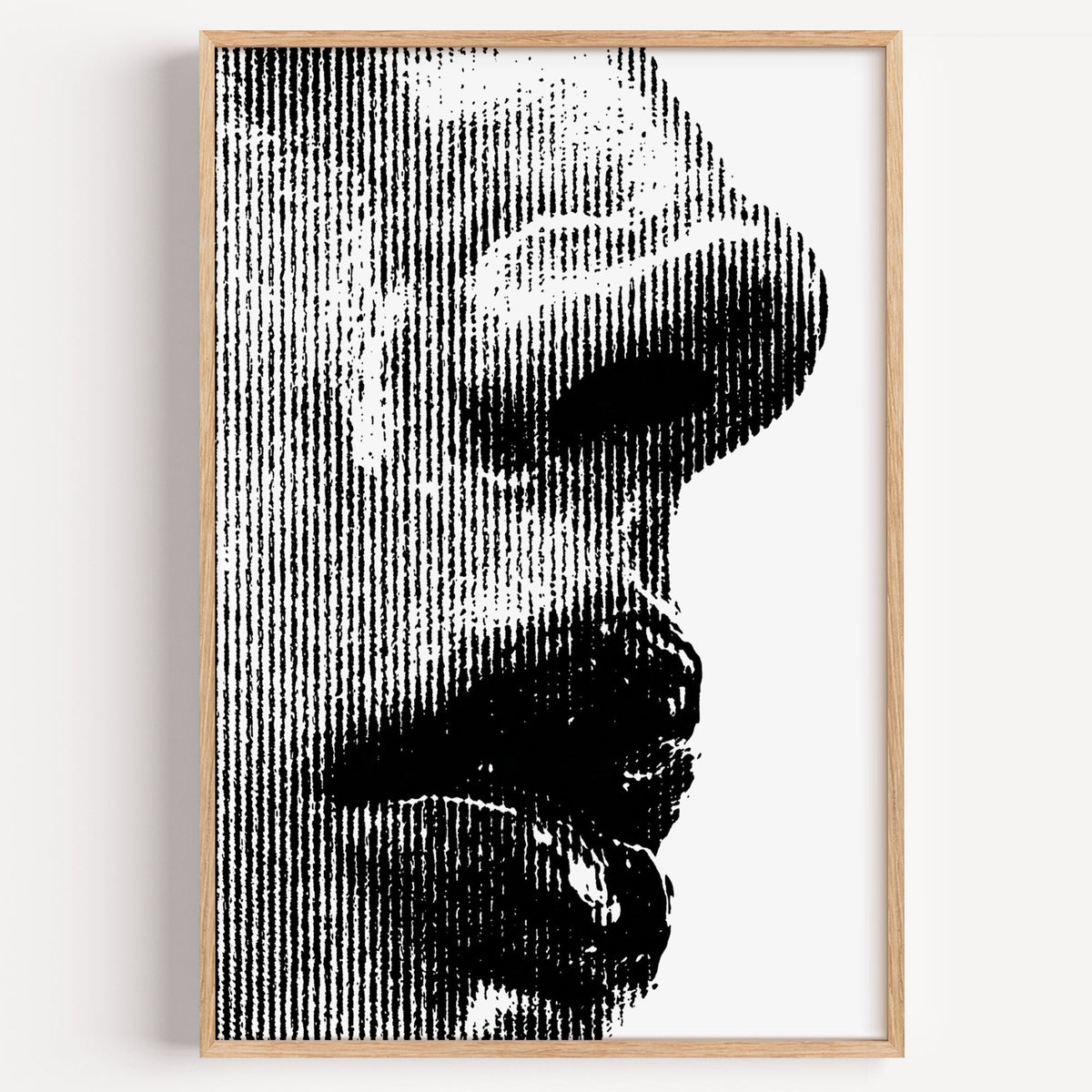 Halftone line face profile graphic print in a light oak frame on a plain white wall
