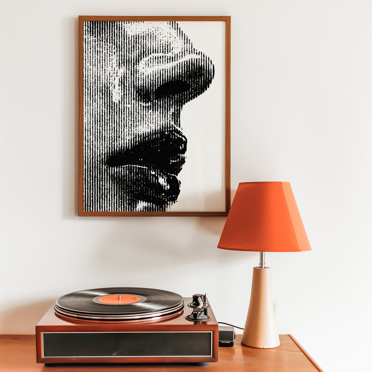 Halftone line face profile graphic print in a walnut frame above a record player and orange lamp