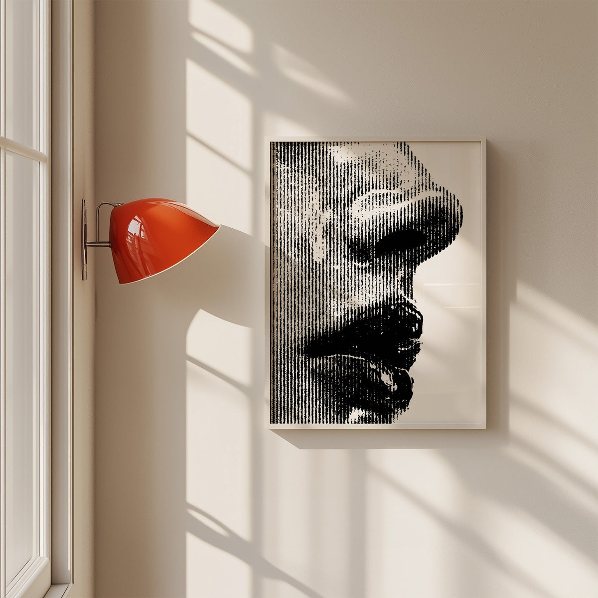Halftone line face profile graphic print in a white frame on a sunlit wall beside a red sconce