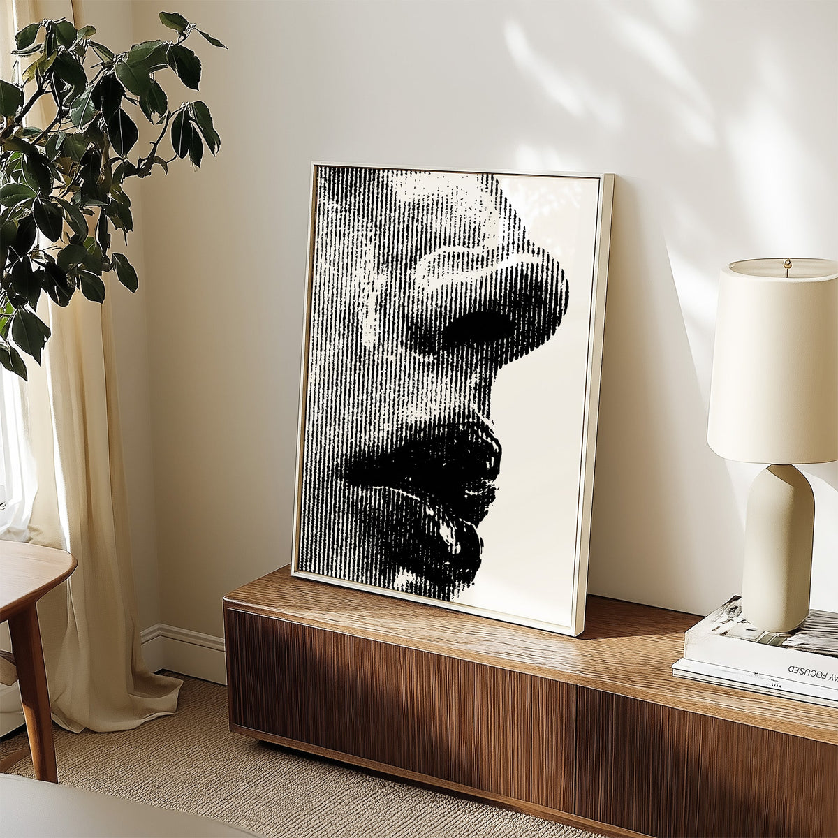 Halftone line face profile graphic print in a white frame on a walnut sideboard beside a ceramic lamp