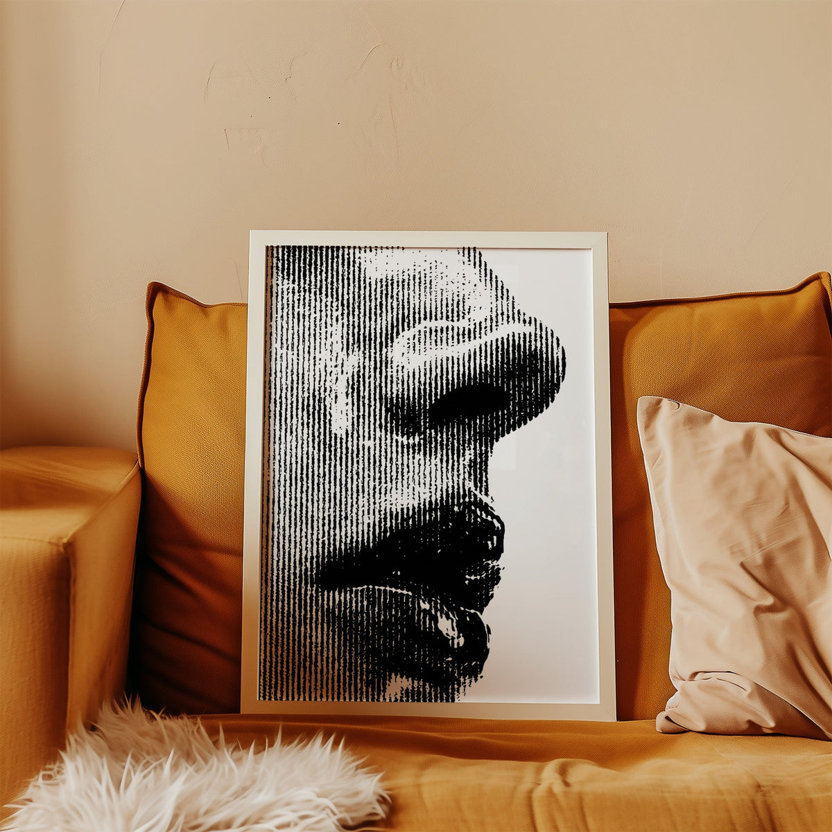 Halftone line face profile graphic print in a white frame leaning on a mustard velvet sofa