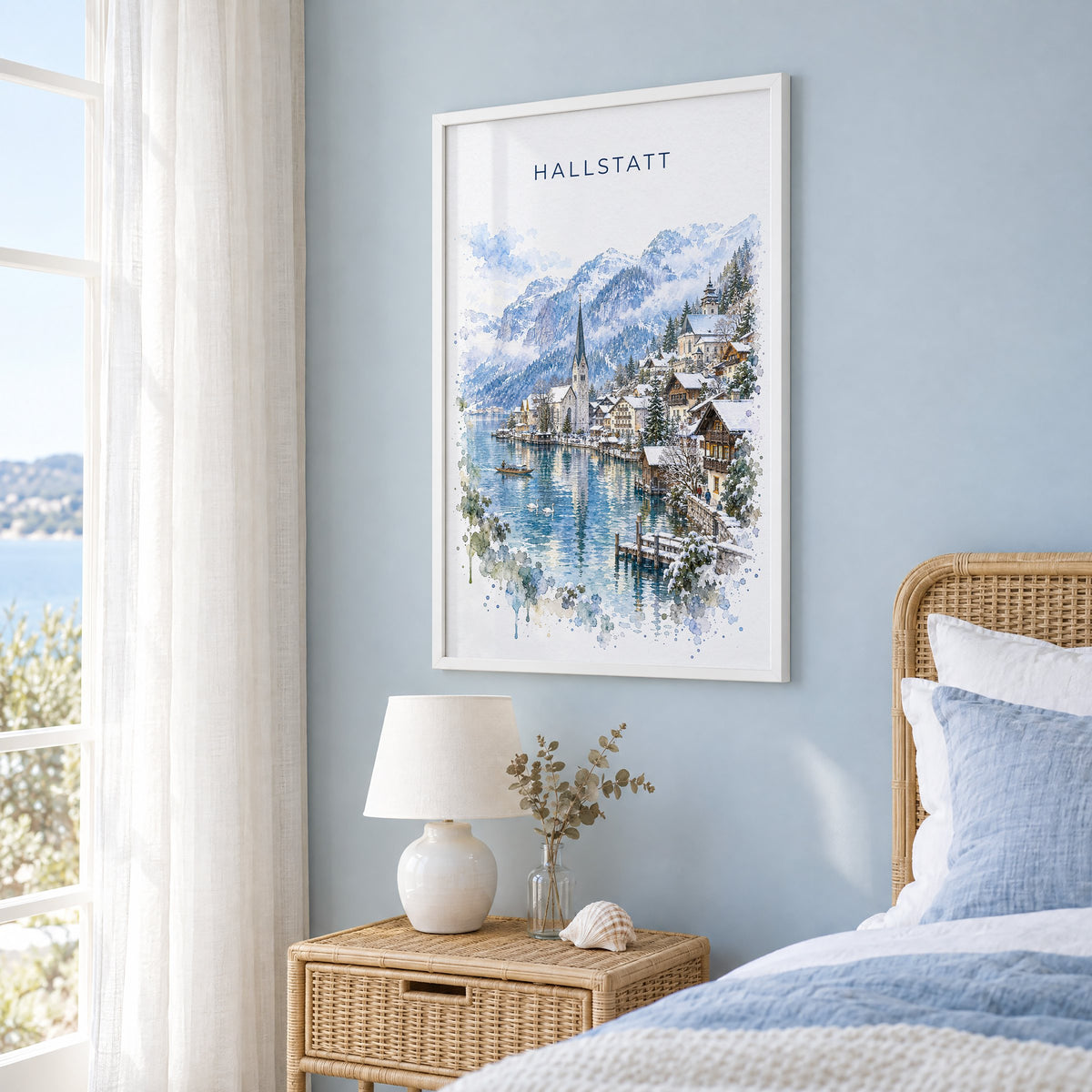 Hallstatt watercolor print in a white frame on a pale blue wall beside a rattan bed in a coastal bedroom
