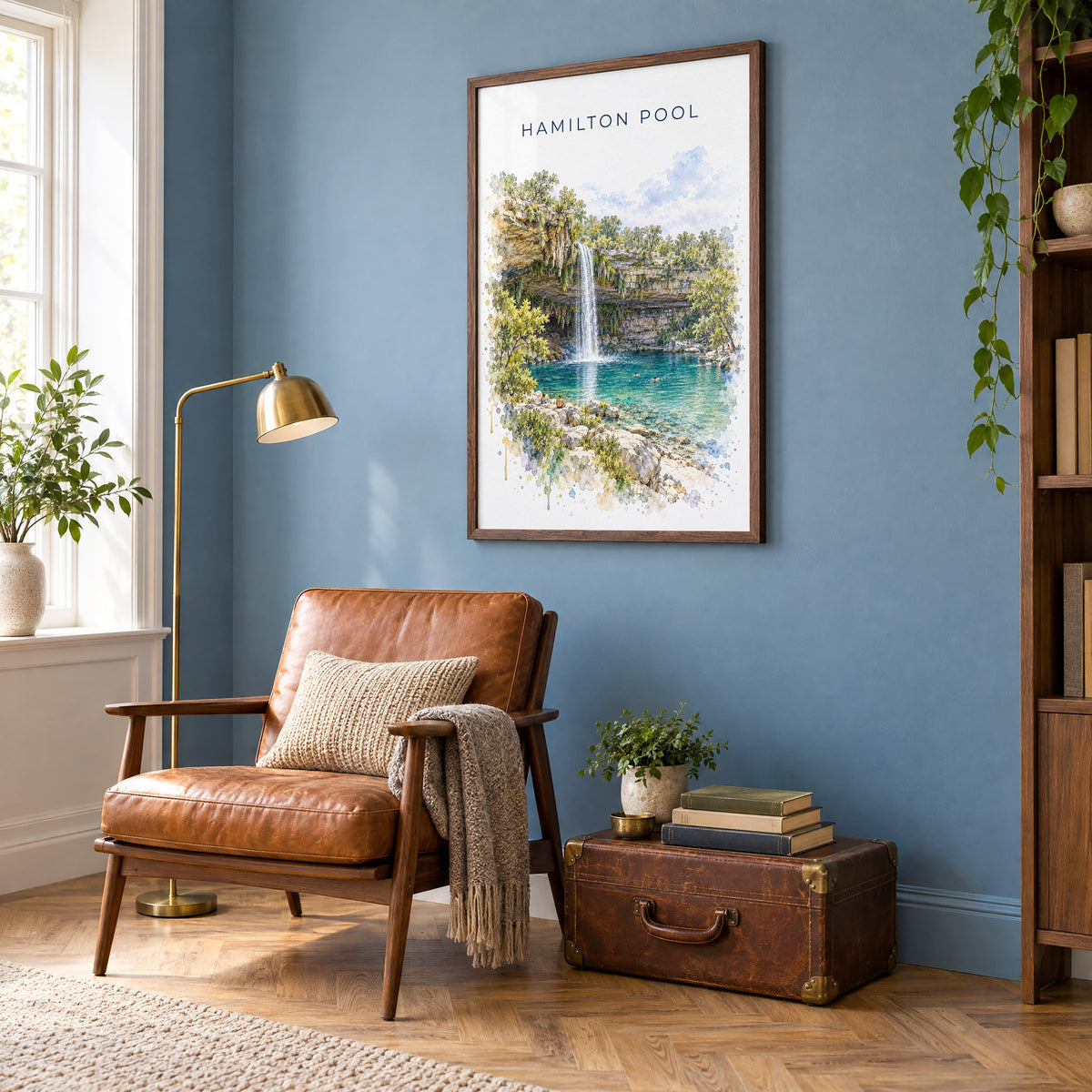 Hamilton Pool watercolor print in a walnut frame on a blue wall above a leather armchair in a reading nook