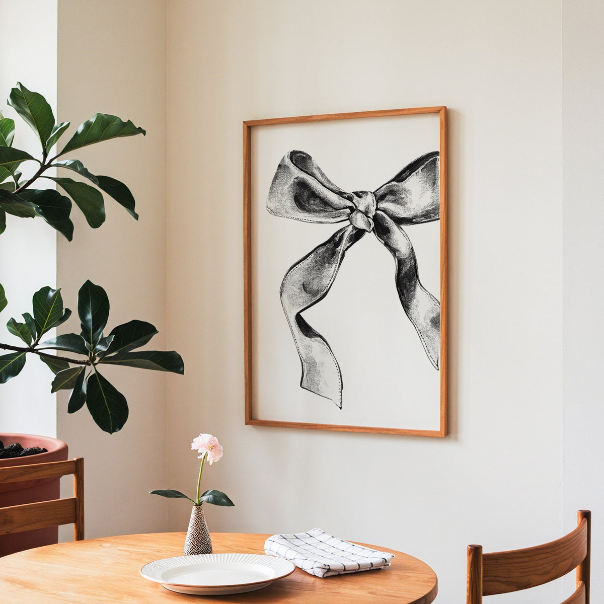 Stippled ink ribbon bow drawing print in a teak frame above a round wooden dining table