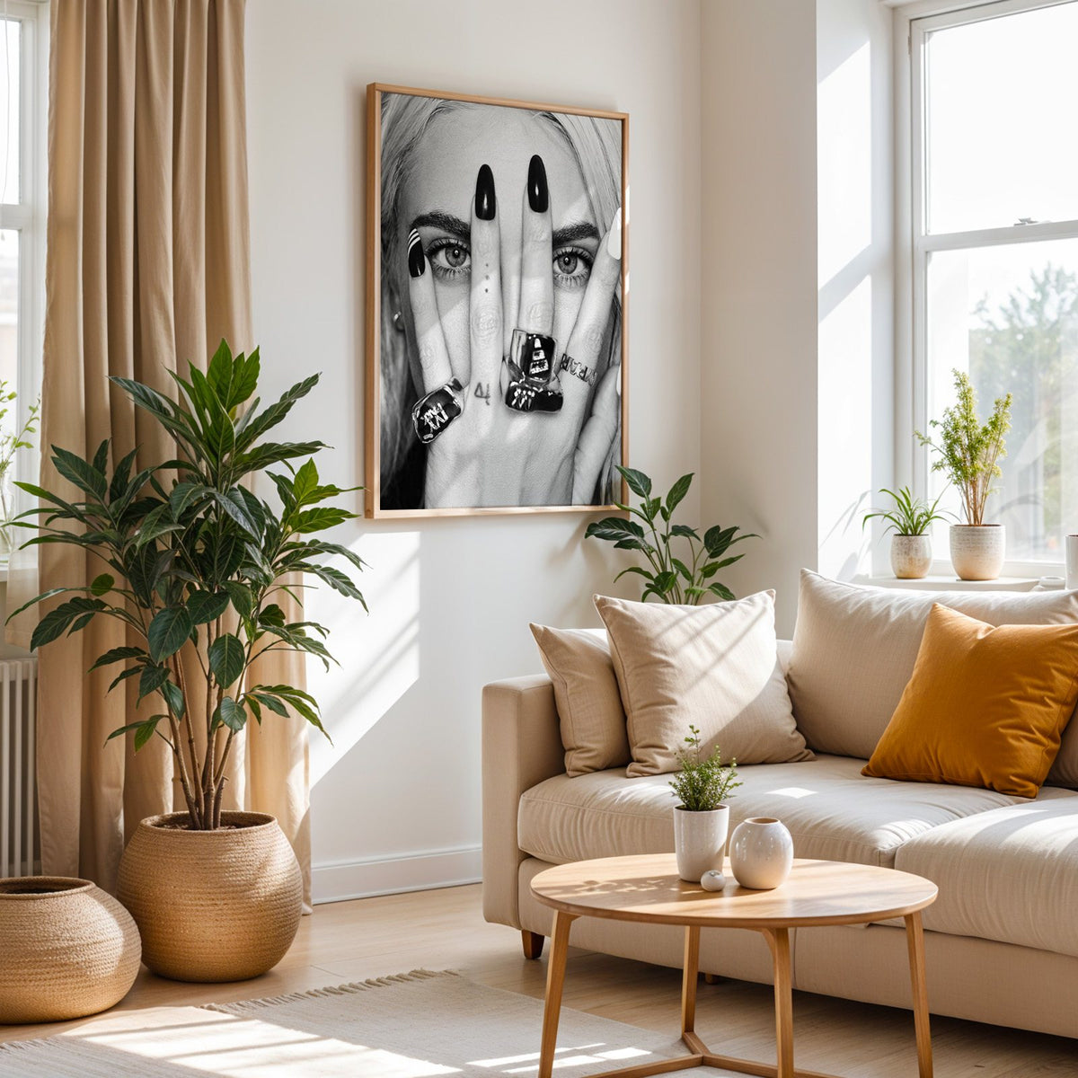 Hand with black nails and rings over eyes print in an oak frame above a cream sofa beside woven planters