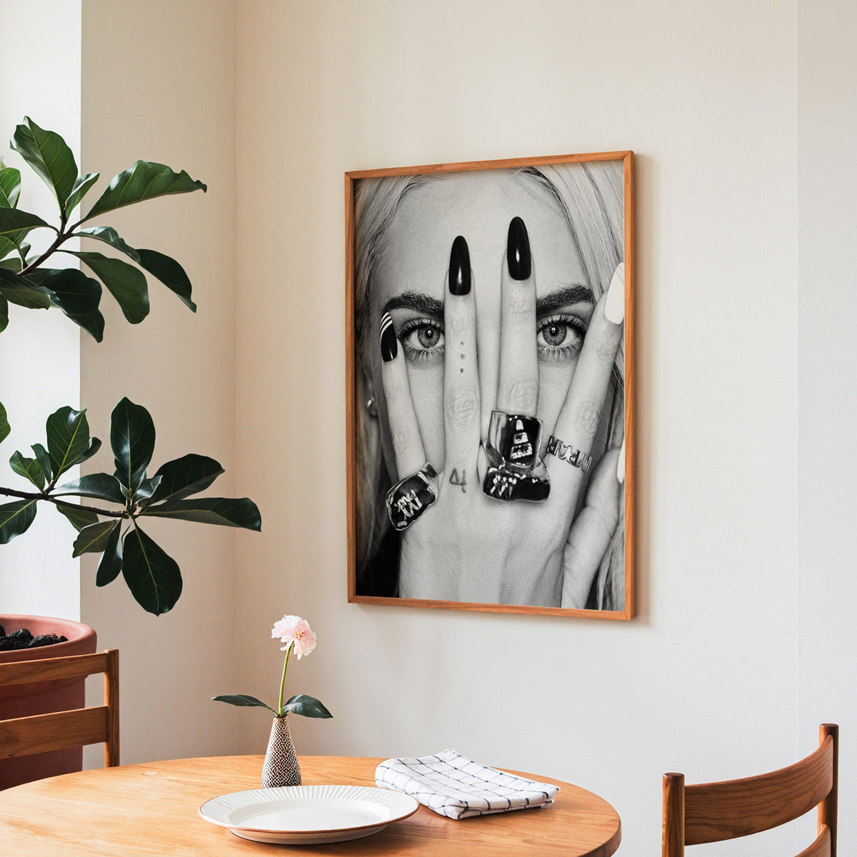 Hand with black nails and rings over eyes print in a teak frame above a round wooden dining table