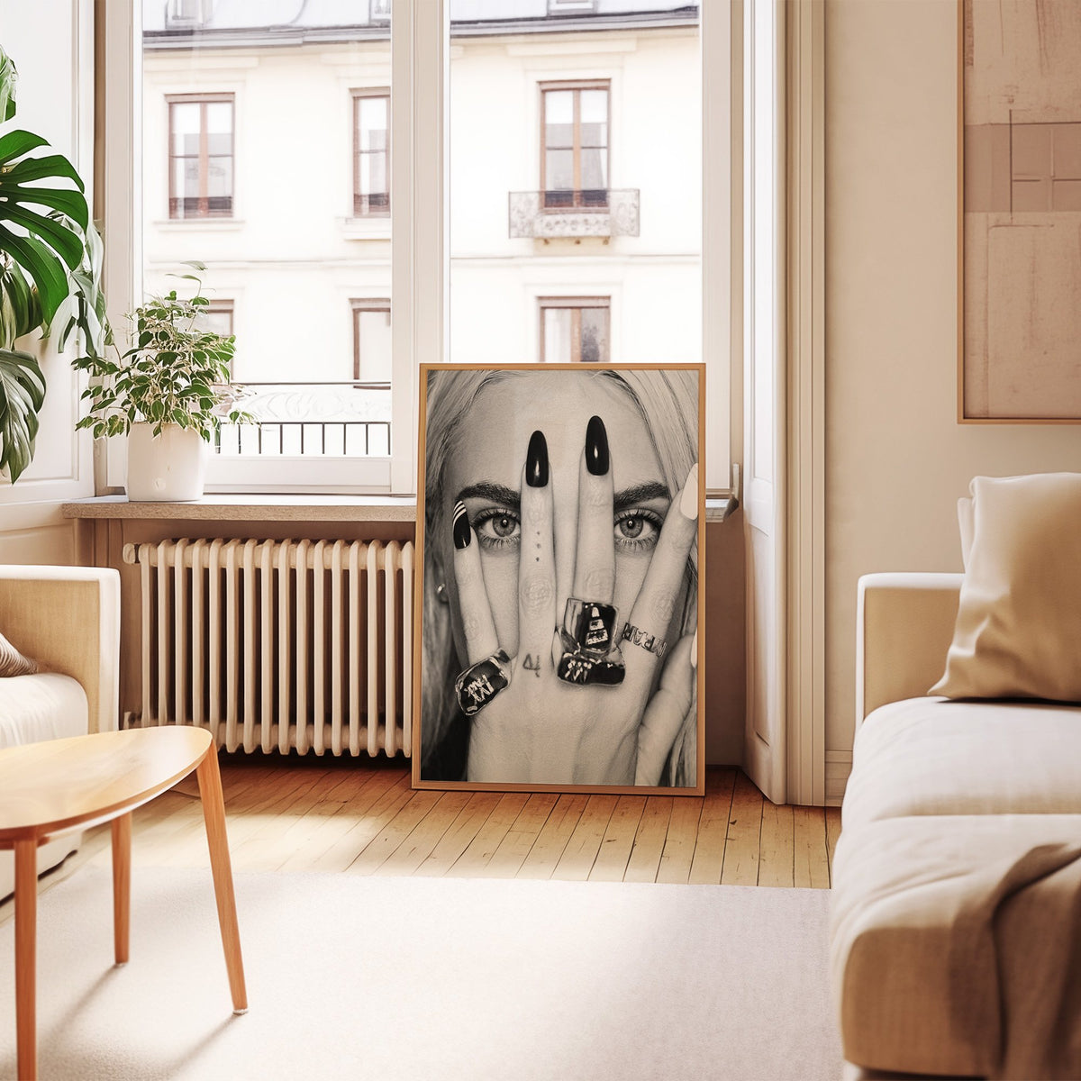 Hand with black nails and rings over eyes print in an oak frame leaning by a French window in a living room