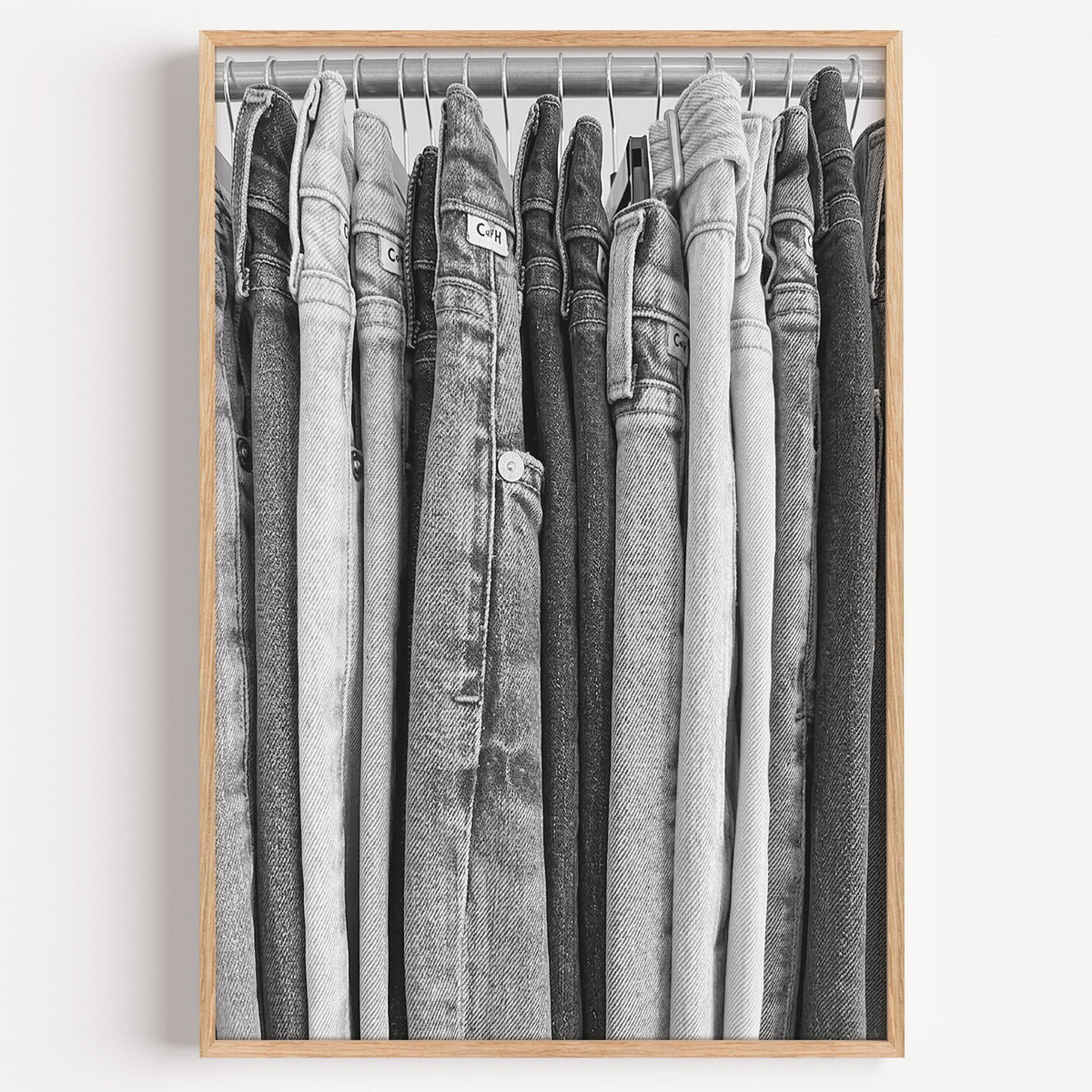 Row of jeans on rack in grey tones print in a light oak frame on a plain white wall