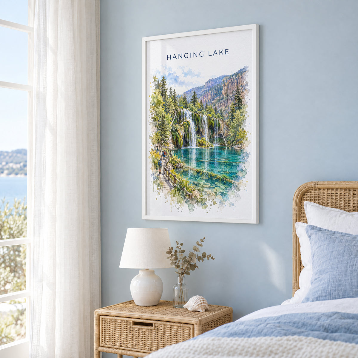 Hanging Lake watercolor print in a white frame on a pale blue wall beside a rattan bed in a coastal bedroom