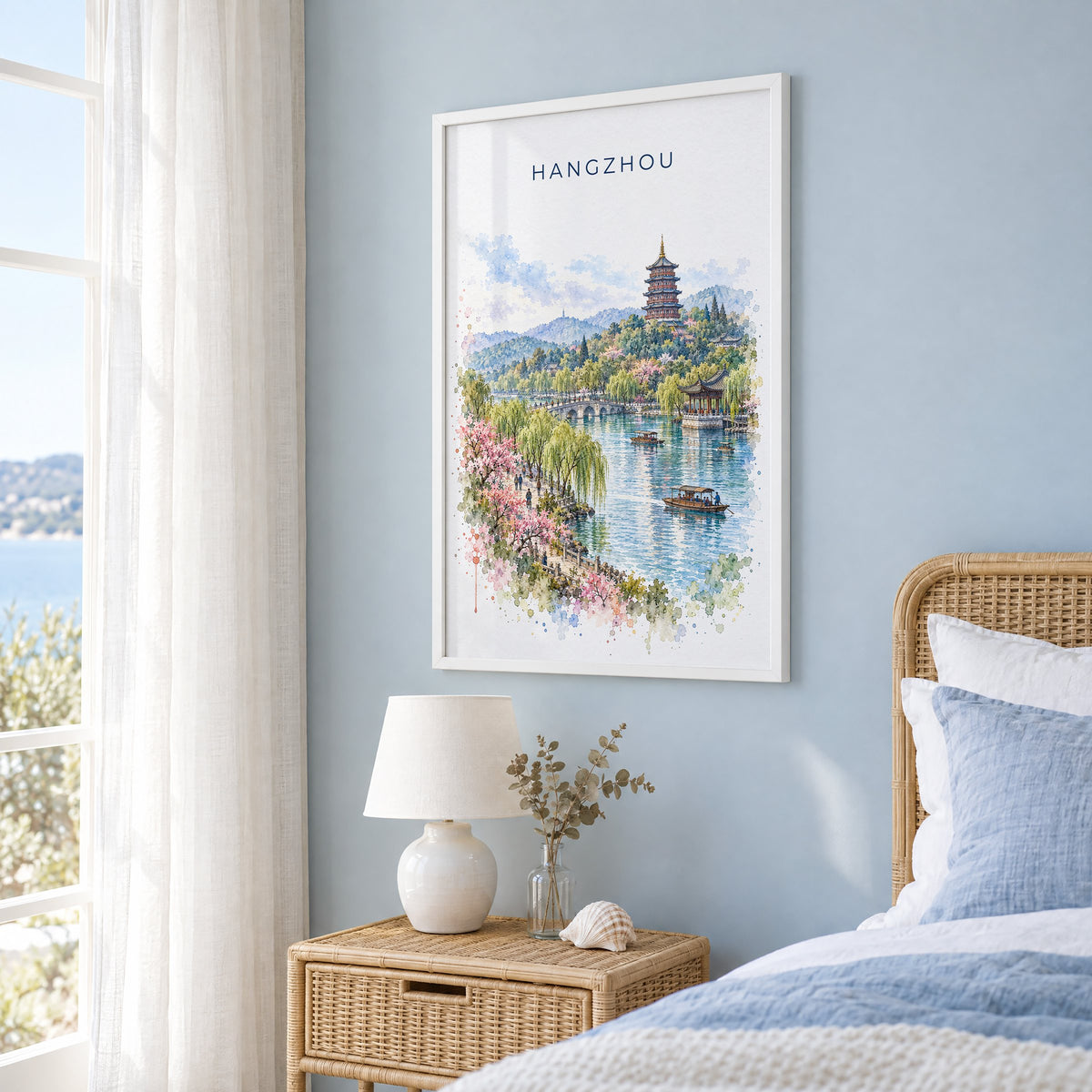 Hangzhou watercolor print in a white frame on a pale blue wall beside a rattan bed in a coastal bedroom