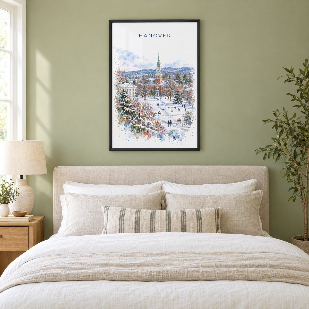 Hanover, New Hampshire watercolor print in a black frame above an upholstered headboard in a sage green bedroom