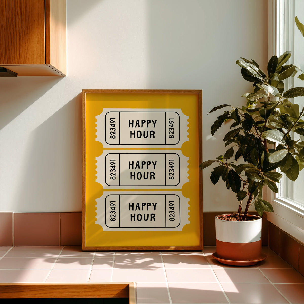 Happy Hour yellow tickets print in a golden oak frame leaning on a pink tiled ledge in strong afternoon sun