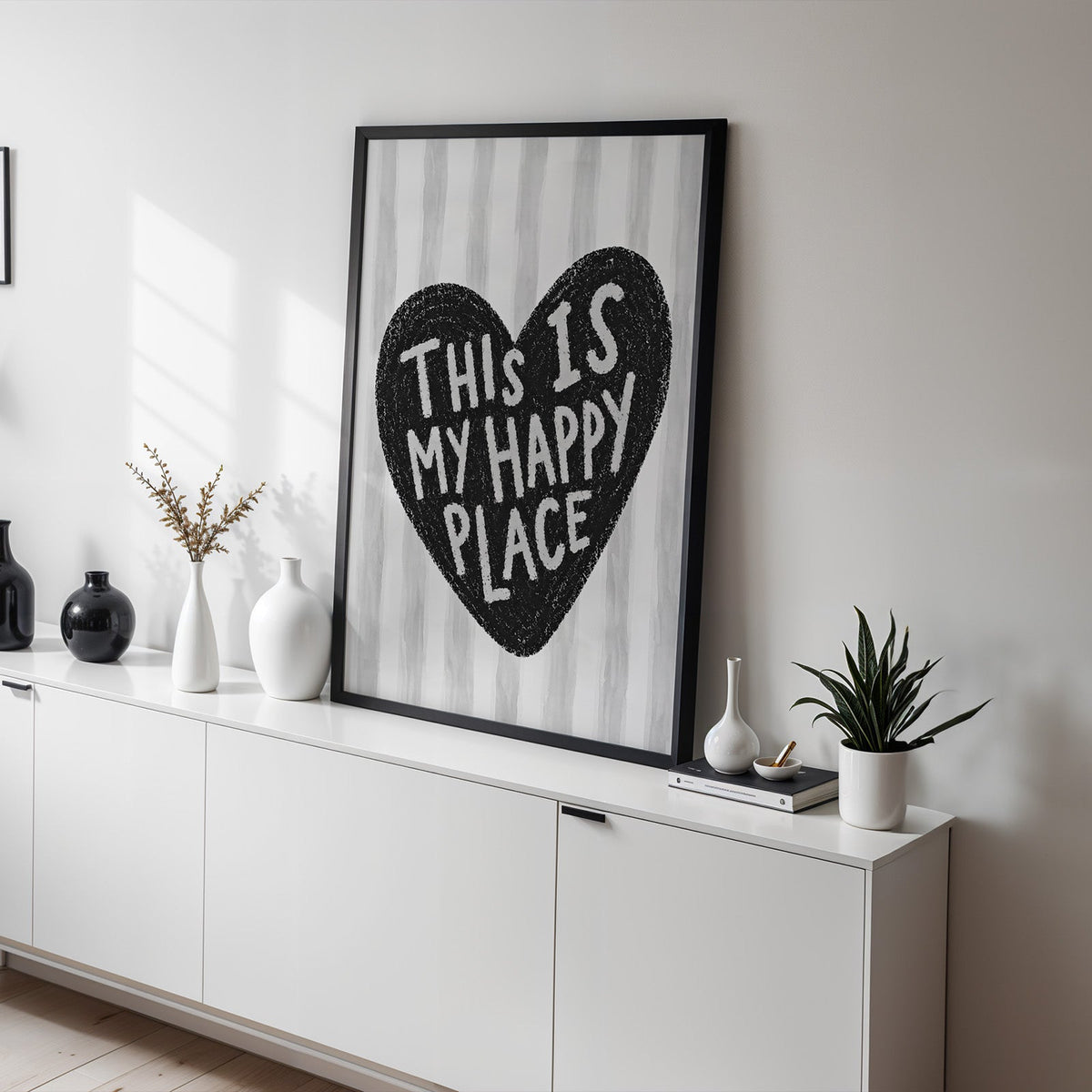 This is my happy place heart quote print in a black frame on a white sideboard with black and white vases