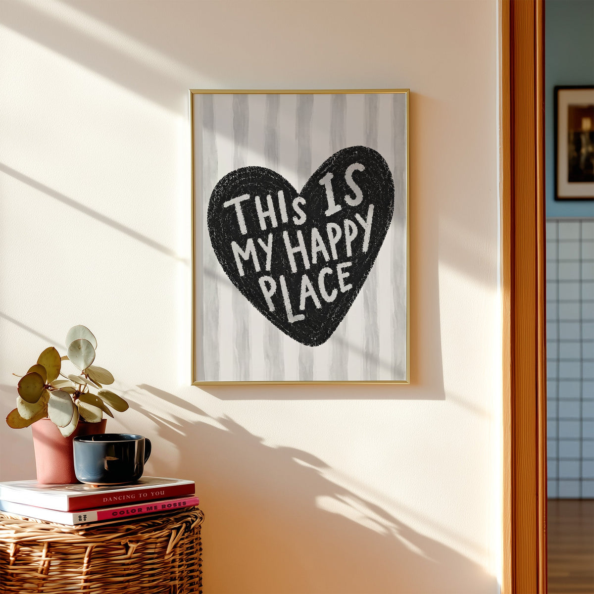 This is my happy place heart quote print shown in a gold frame above a wicker basket and stacked books