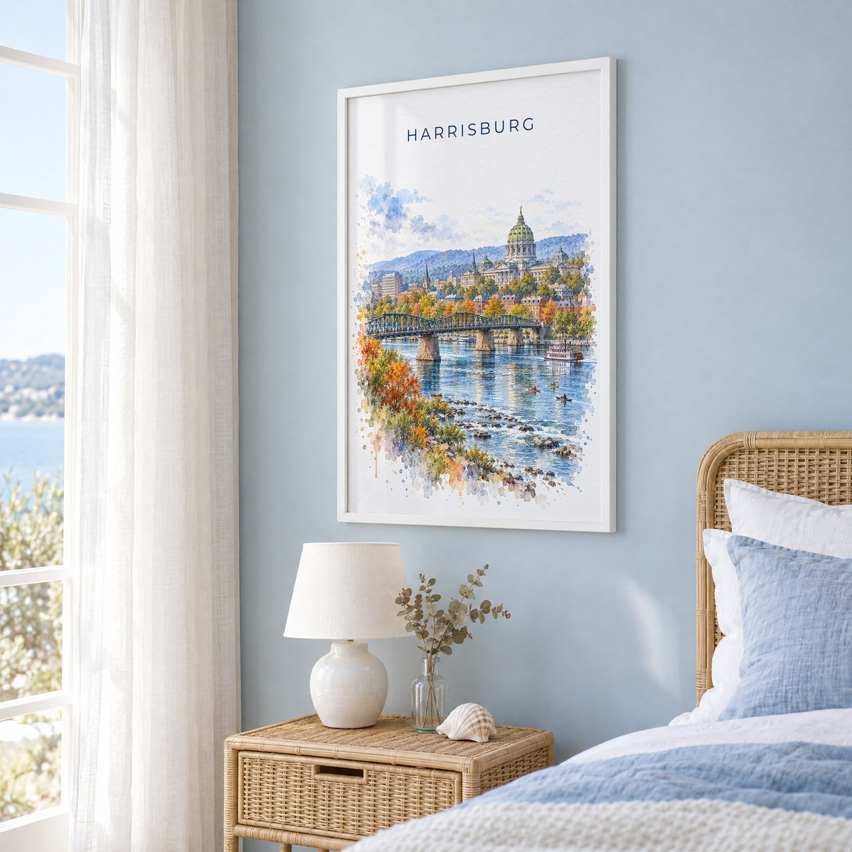 Harrisburg watercolor print in a white frame on a pale blue wall beside a rattan bed in a coastal bedroom