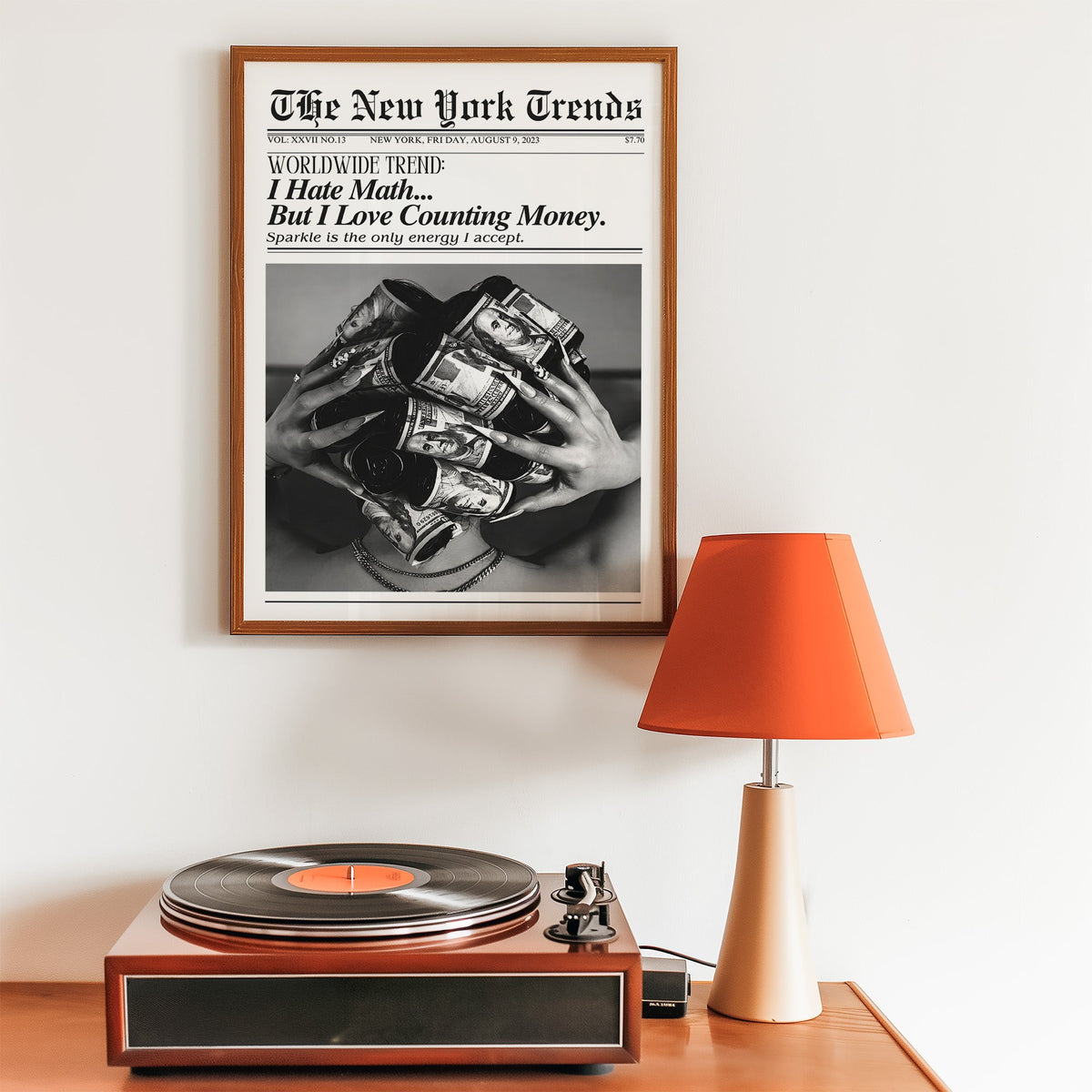 Dollar bill hair rollers mock newspaper print in a walnut frame above a record player and orange lamp
