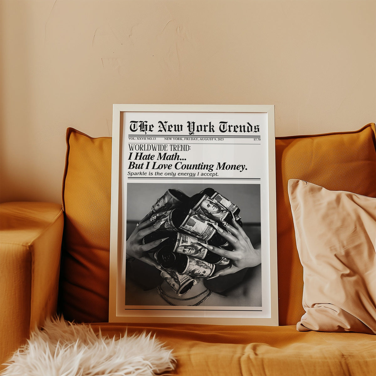 Dollar bill hair rollers mock newspaper print in a white frame leaning on a mustard velvet sofa