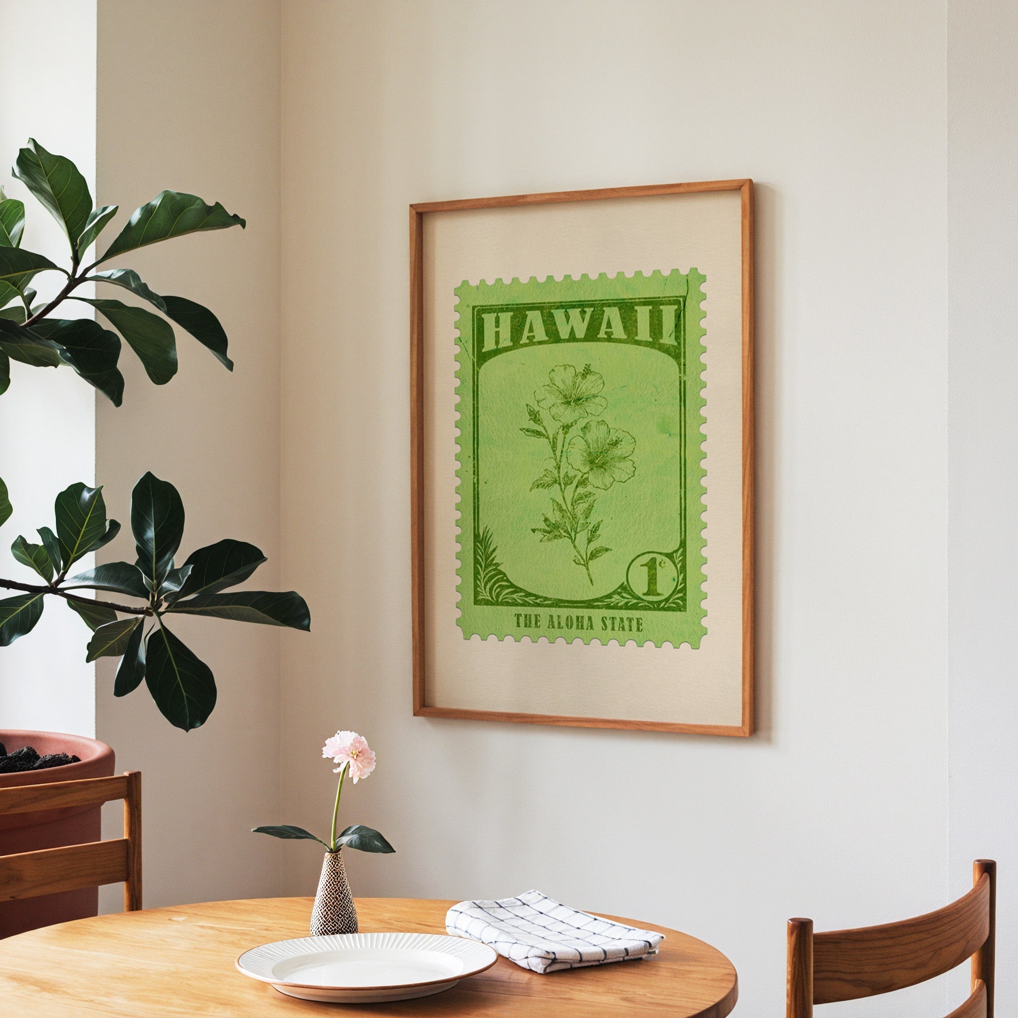Hawaii state flower print framed above a round wooden table with a single bloom in a vase and books
