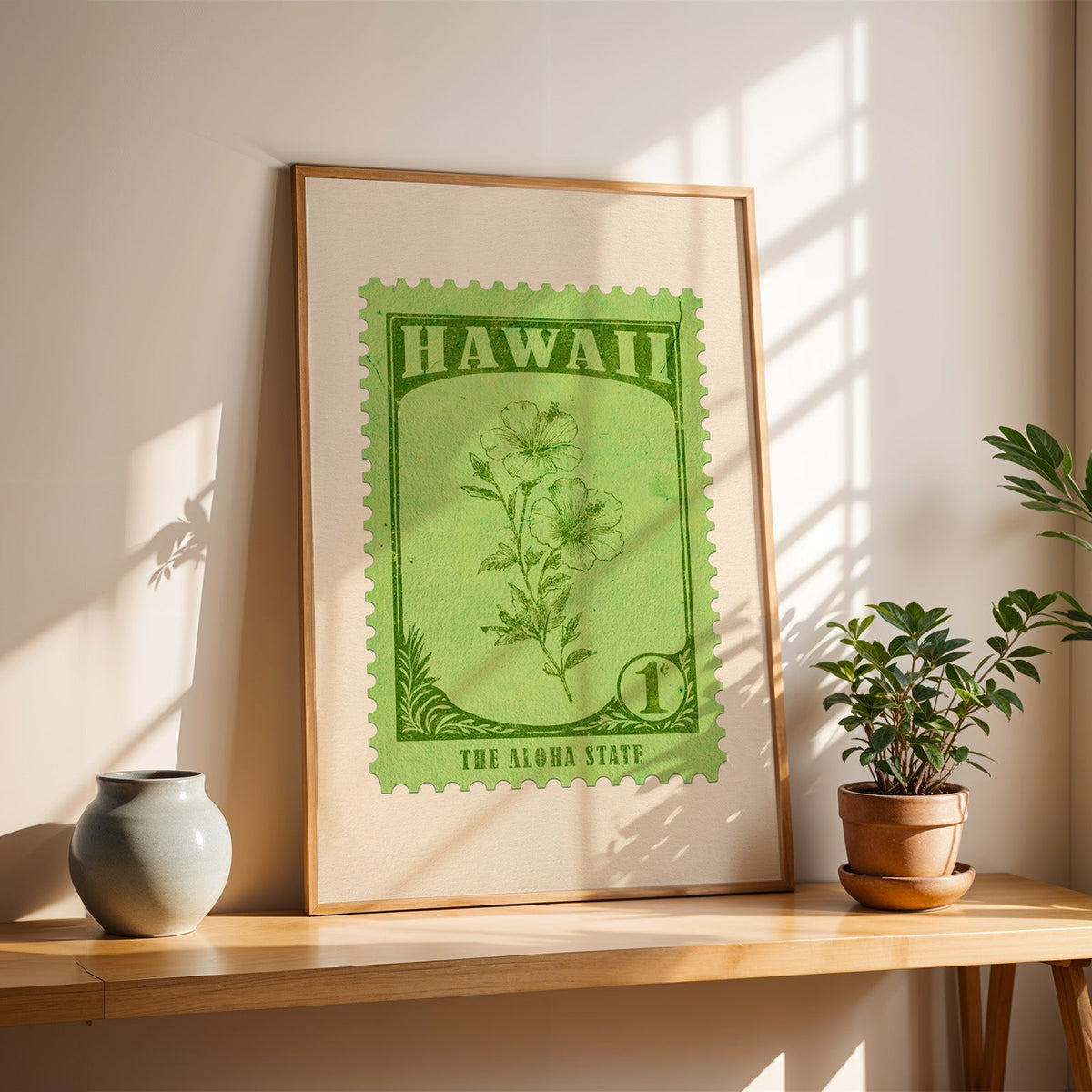 Hawaii yellow hibiscus stamp print in a light oak frame leaning on a wooden table beside a stoneware vase