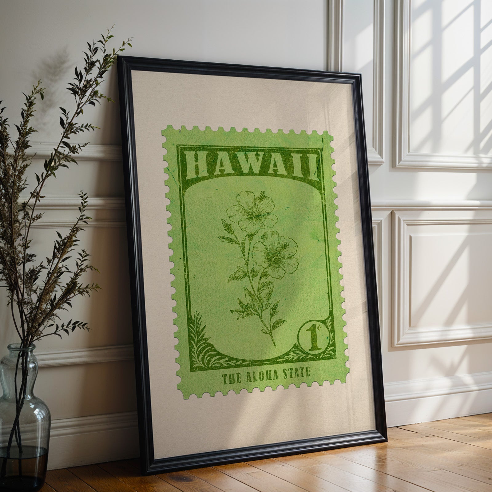 Hawaii state flower print in a black frame leaning against a white panelled wall beside olive branches