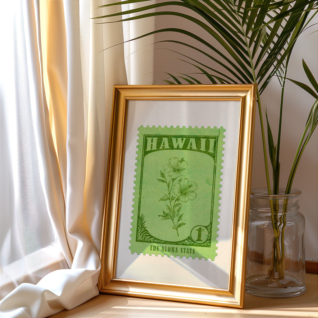 Hawaii stamp print in a gold frame leaning by a cream curtain with a palm in a glass jar