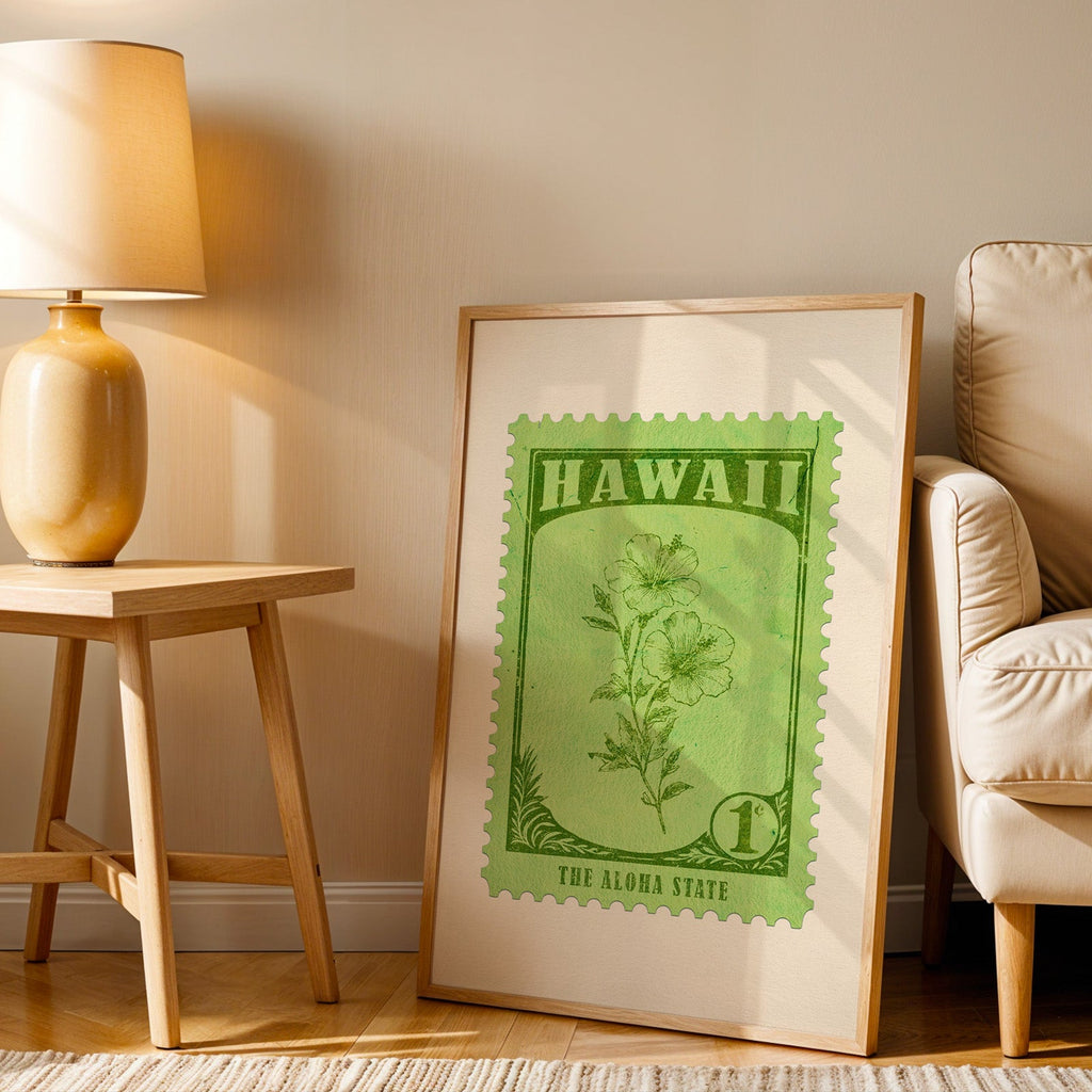 Hawaii stamp print in a wood frame resting on the floor beside a beige armchair and a yellow lamp