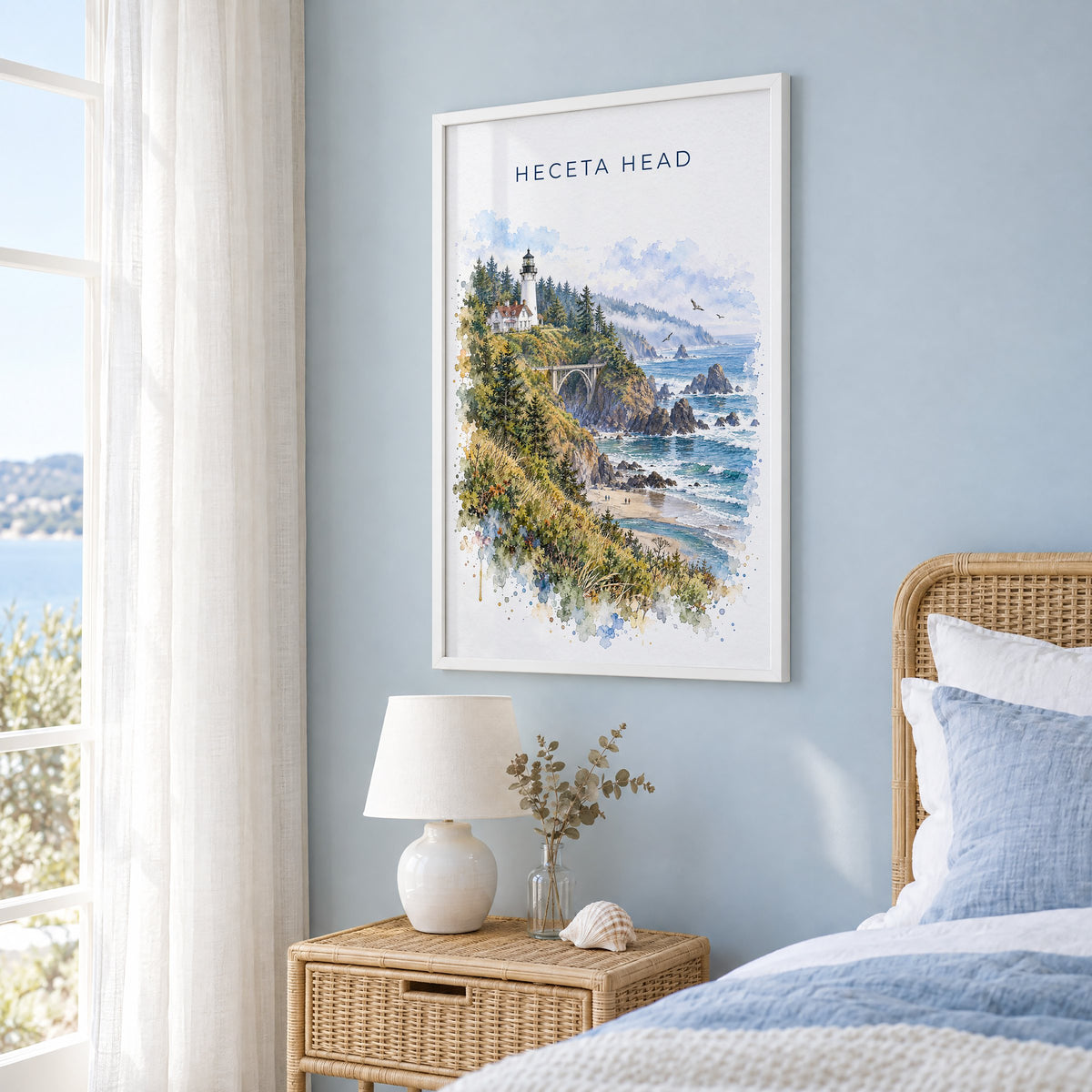 Heceta Head watercolor print in a white frame on a pale blue wall beside a rattan bed in a coastal bedroom