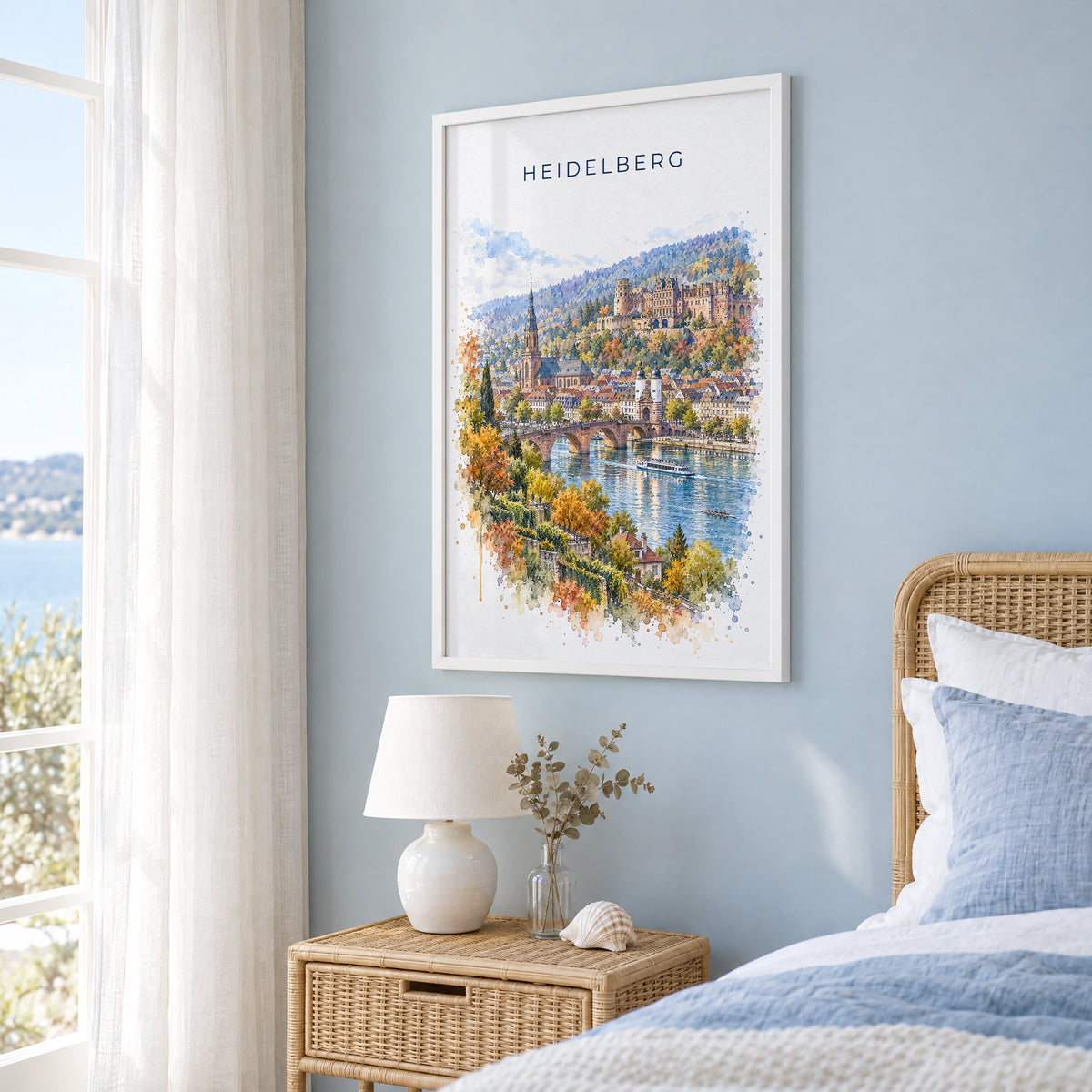 Heidelberg watercolor print in a white frame on a pale blue wall beside a rattan bed in a coastal bedroom