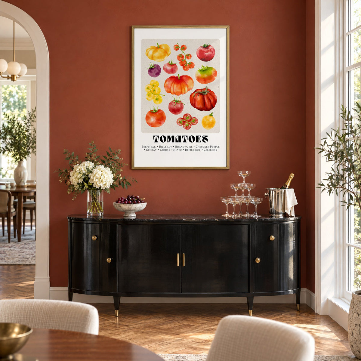 Tomato varieties watercolor print in a brass frame on a terracotta wall above a black buffet with a champagne tower
