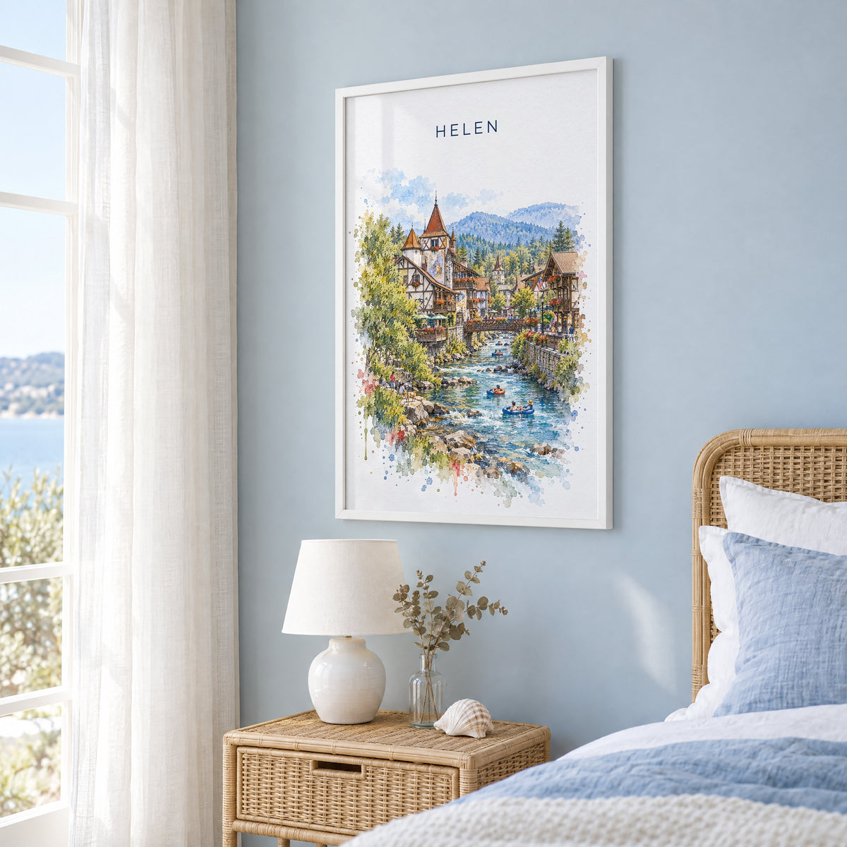 Helen, Georgia watercolor print in a white frame on a pale blue wall beside a rattan bed in a coastal bedroom