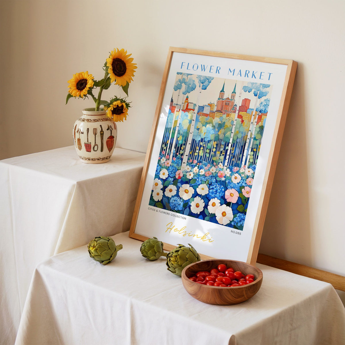 Helsinki flower market print in an oak frame leaning on a linen-draped table beside a vase of sunflowers