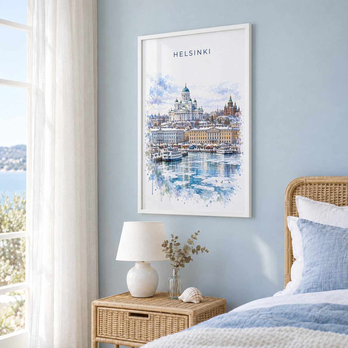 Helsinki watercolor print in a white frame on a pale blue wall beside a rattan bed in a coastal bedroom