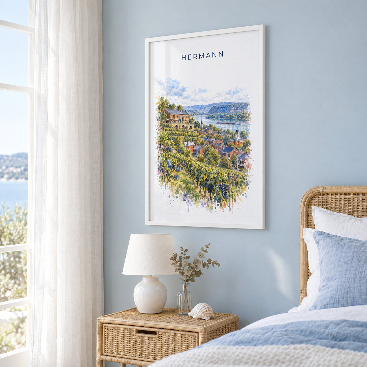 Hermann, Missouri watercolor print in a white frame on a pale blue wall beside a rattan bed in a coastal bedroom