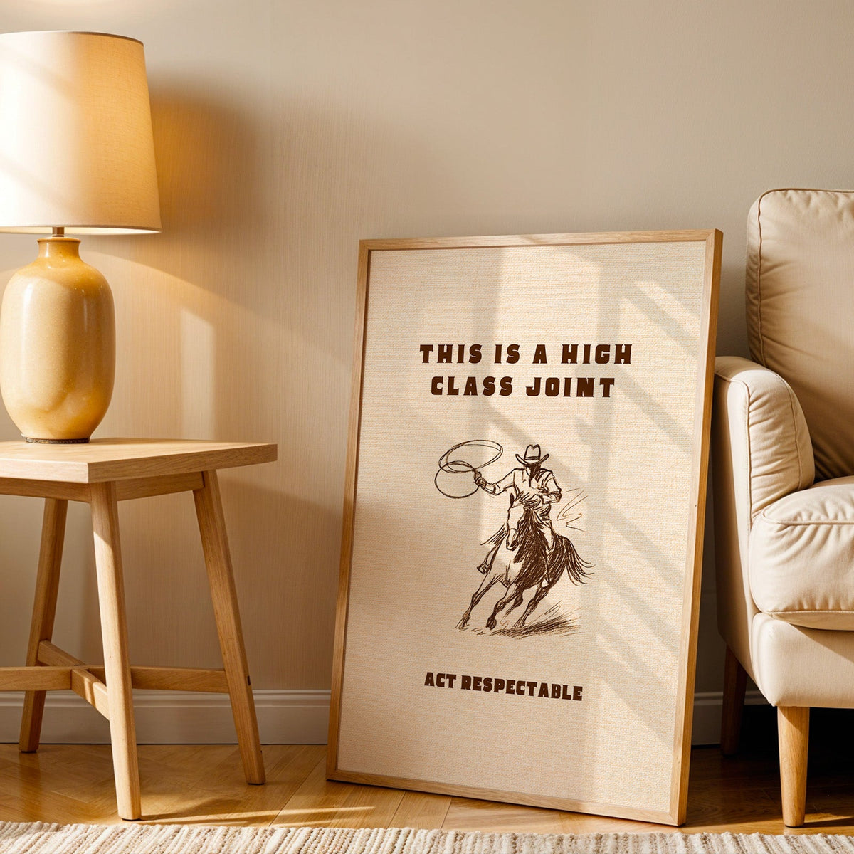 High Class Joint cowgirl cream print in an oak frame beside an amber ceramic lamp