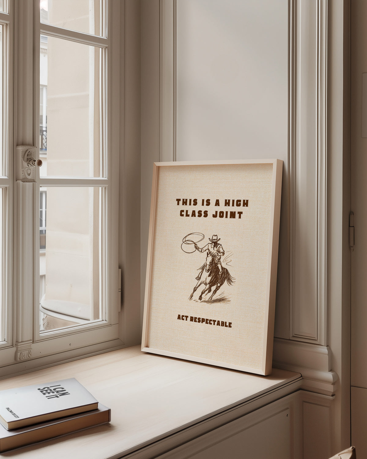 High Class Joint cowgirl cream print in a pale wood frame on a sunlit window ledge