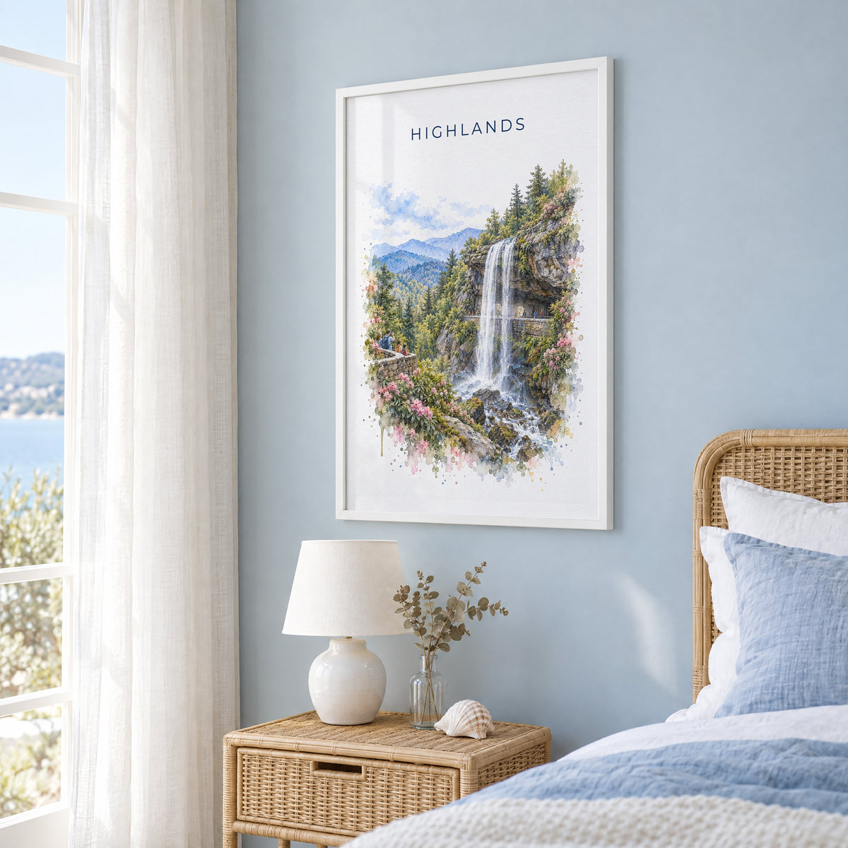 Highlands, North Carolina watercolor print in a white frame on a pale blue wall beside a rattan bed in a coastal bedroom