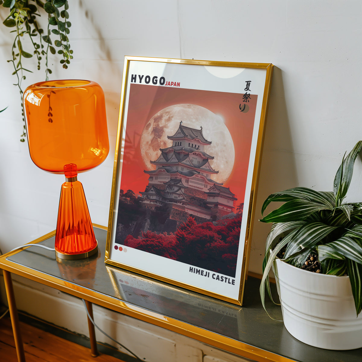 Himeji Castle red moon print shown in a gold frame on a console beside an orange glass lamp