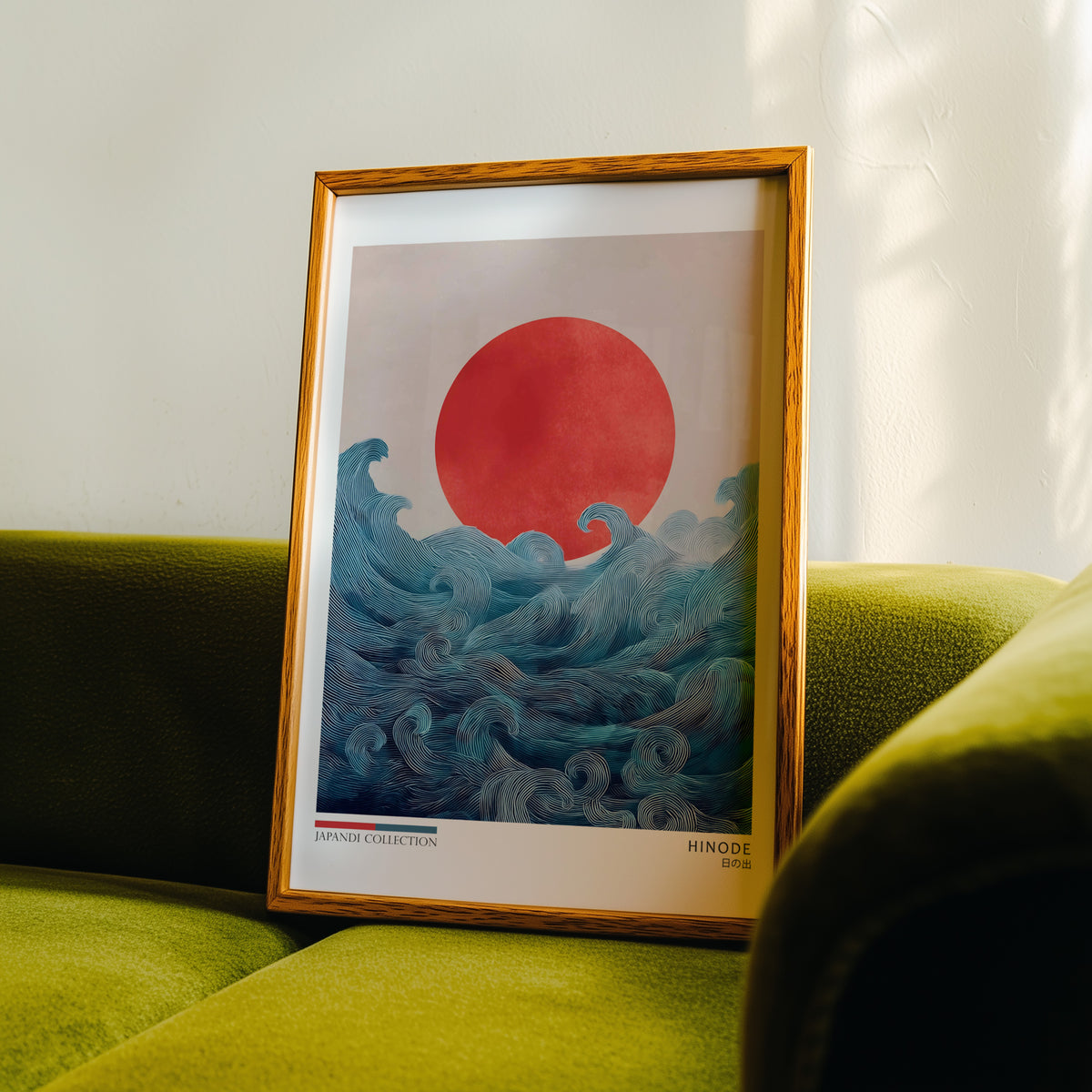 Hinode red sun over waves print in an oak frame propped on a green velvet sofa