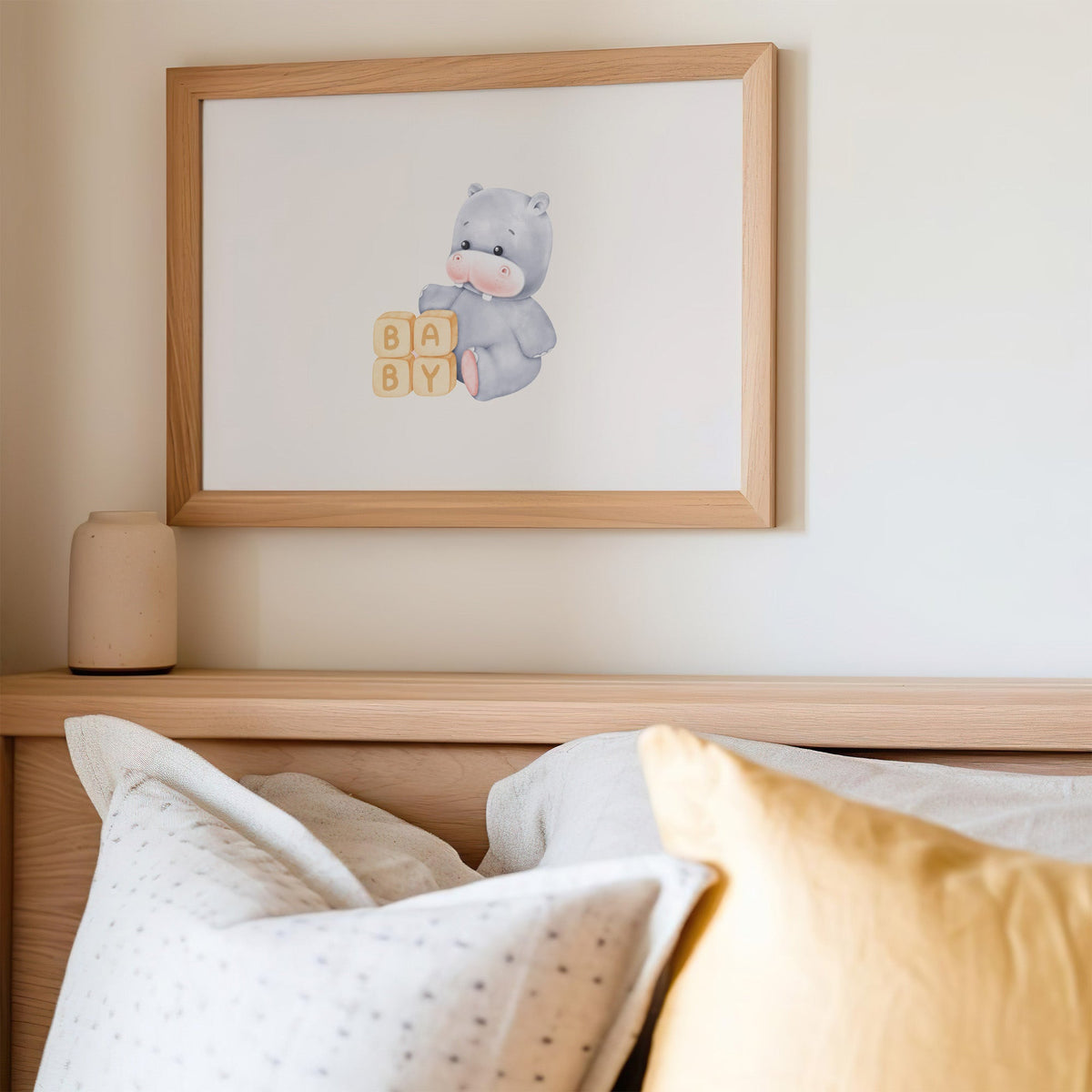 Baby hippo beside wooden BABY blocks nursery print in an oak frame above a wooden headboard with a mustard pillow