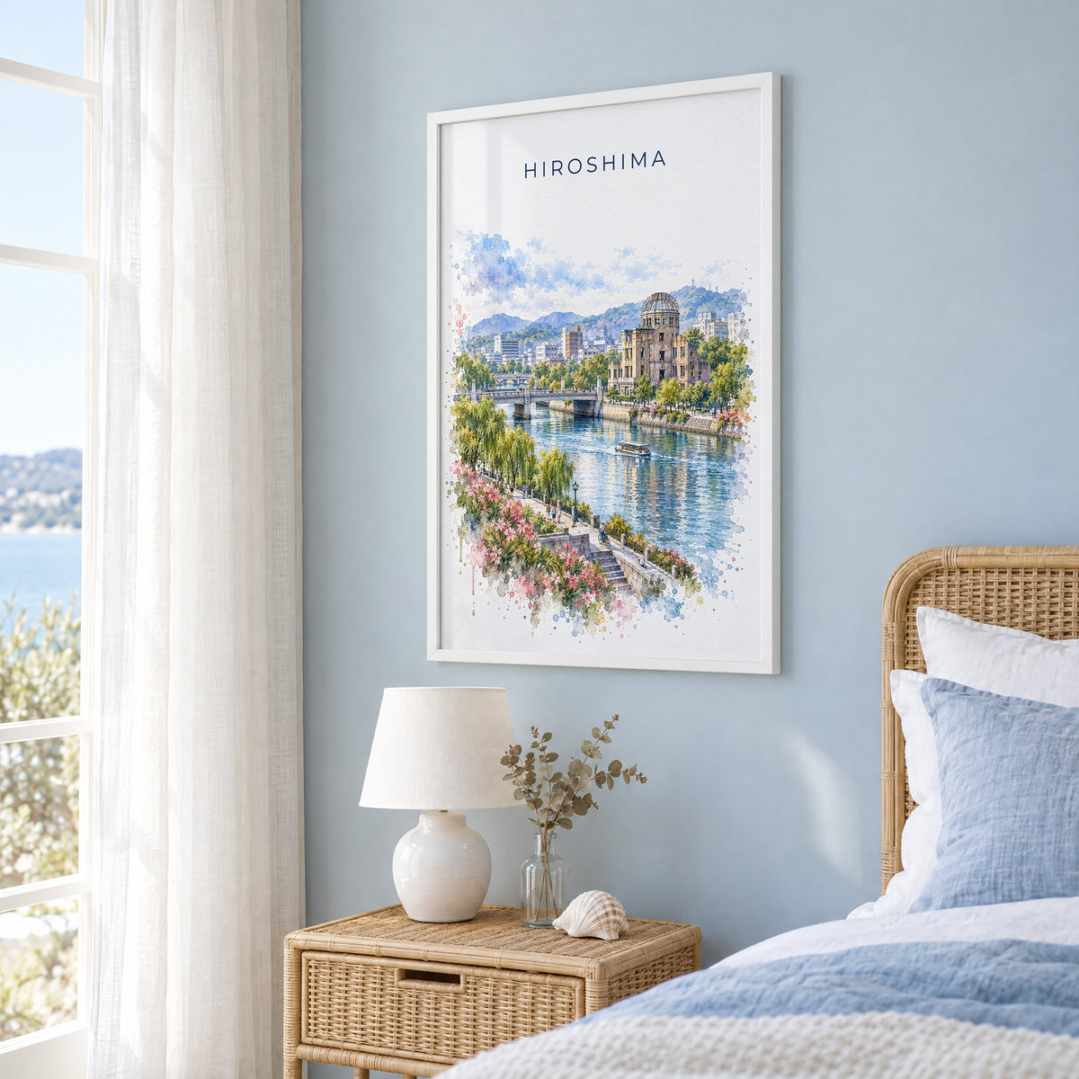 Hiroshima watercolor print in a white frame on a pale blue wall beside a rattan bed in a coastal bedroom