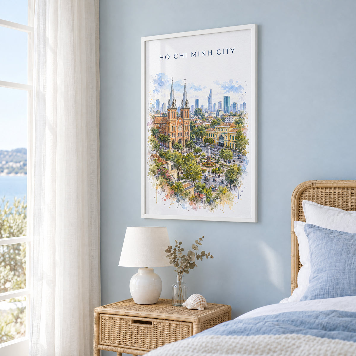 Ho Chi Minh City watercolor print in a white frame on a pale blue wall beside a rattan bed in a coastal bedroom