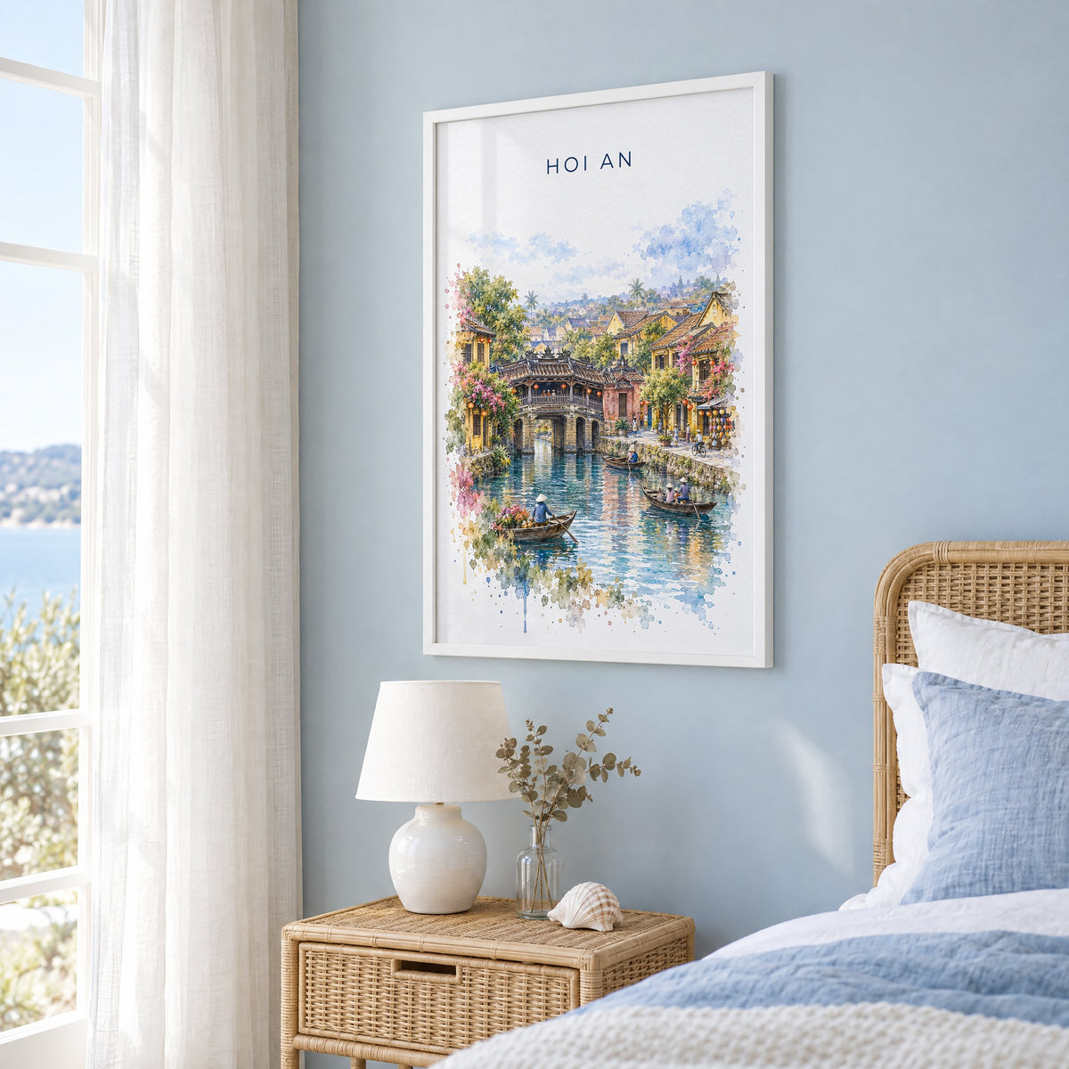 Hoi An watercolor print in a white frame on a pale blue wall beside a rattan bed in a coastal bedroom