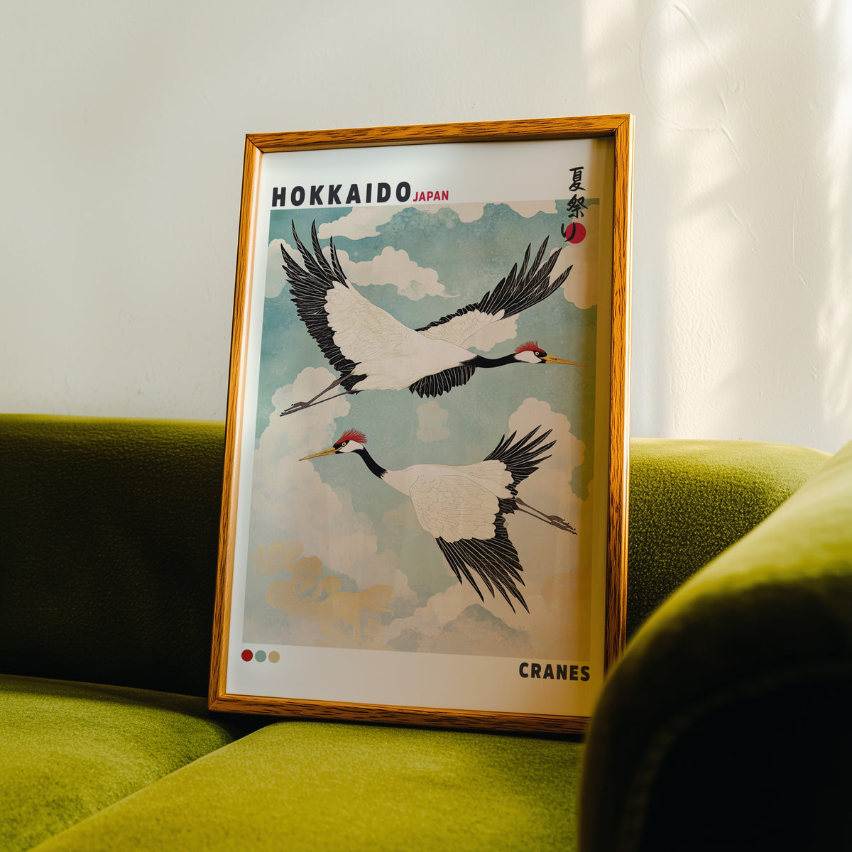 Hokkaido red-crowned cranes in flight print in an oak frame propped on a green velvet sofa