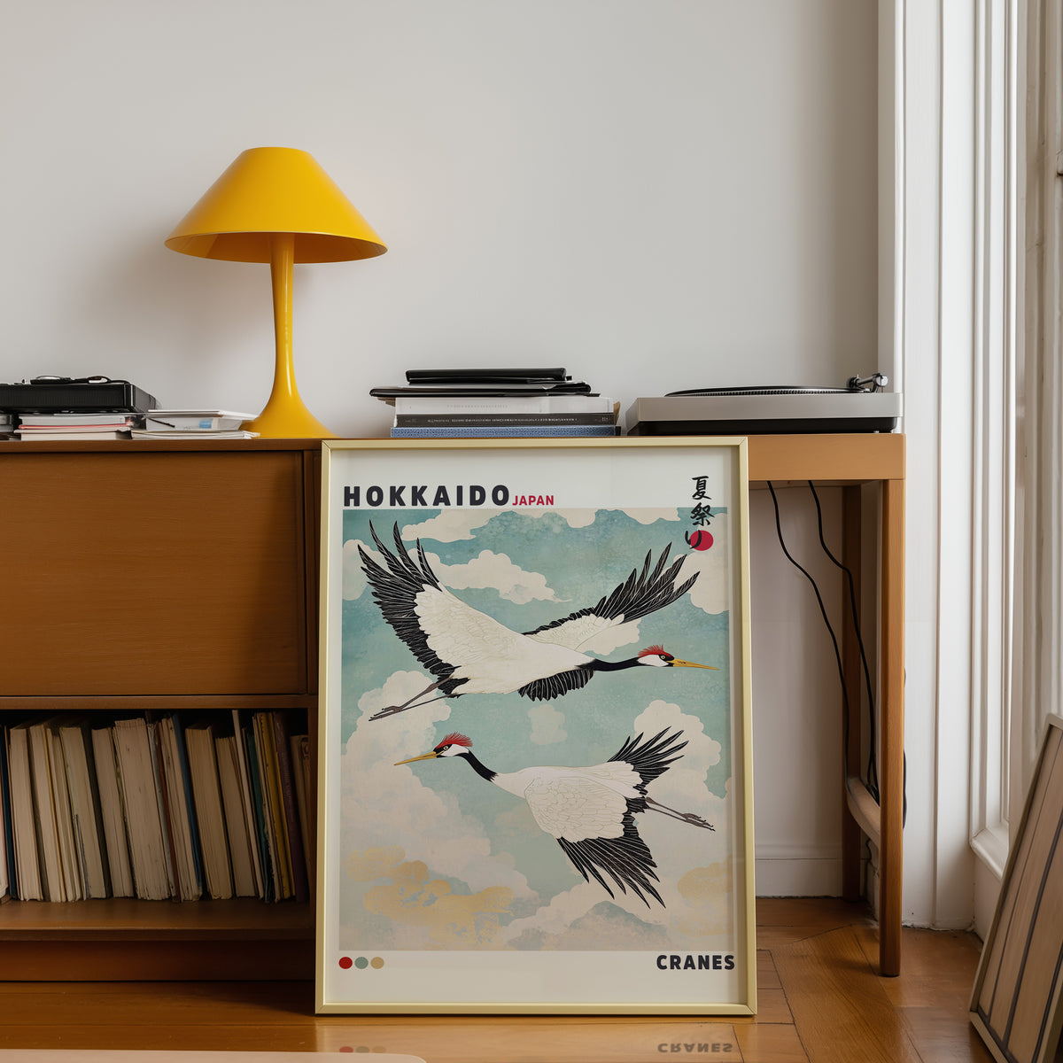 Hokkaido red-crowned cranes in flight print shown in a gold frame below a teak desk with a yellow lamp